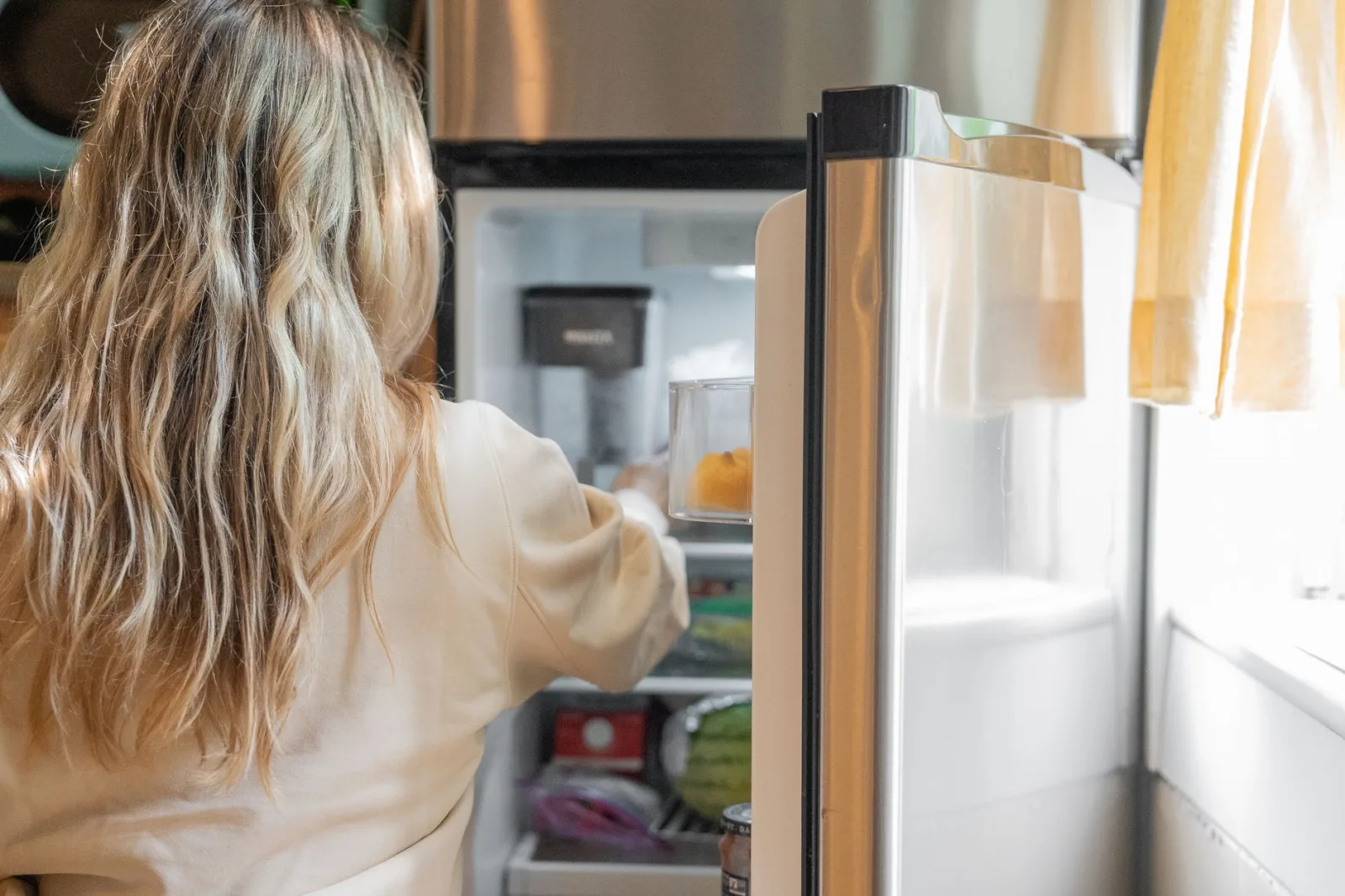 Kobieta wyciąga produkty z otwartej lodówki, widoczne półki i szuflady
