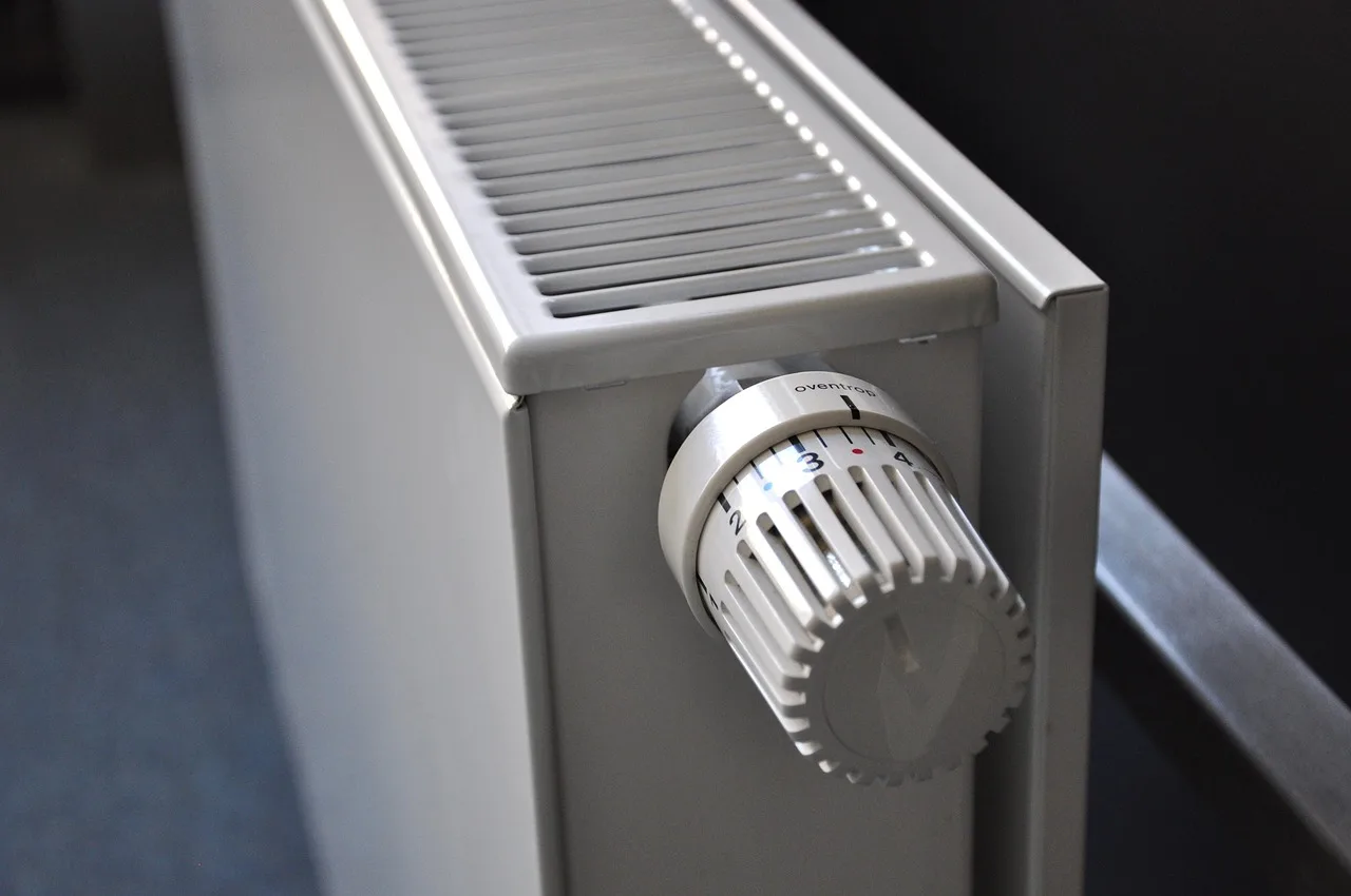 Biały grzejnik płytowy z widoczną głowicą termostatyczną w mieszkaniu